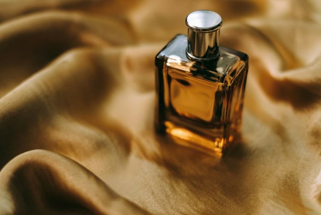 Luxury perfume bottle on draped gold silk - amber liquid, silver cap, no visible branding